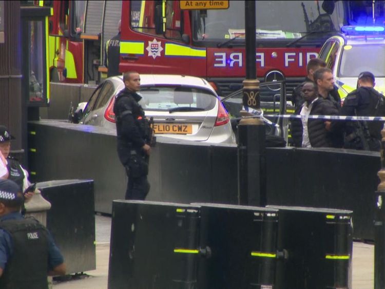 A silver car is surrounded by police and a man appears to be held next to the House of Parliament